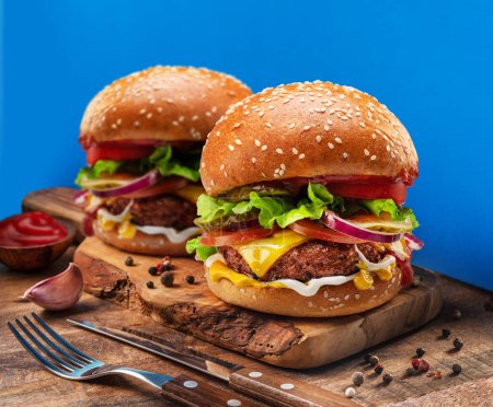 Foto de Sabrosas hamburguesas con queso o hamburguesas en bandeja de madera de cerca. Fondo azul. - Imagen libre de derechos