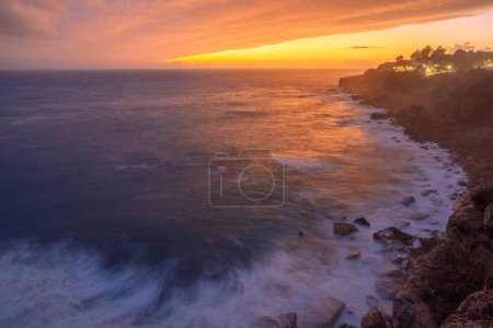 Foto de Puesta de sol colorida roja y cielo dramático vívido en la orilla rocosa del océano Atlántico. - Imagen libre de derechos