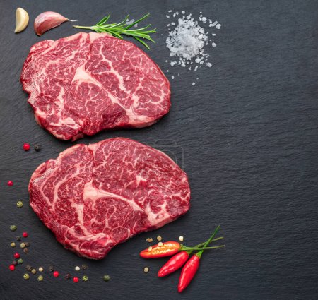 Photo for Raw ribeye steak on stone black serving plate. Flat lay. - Royalty Free Image