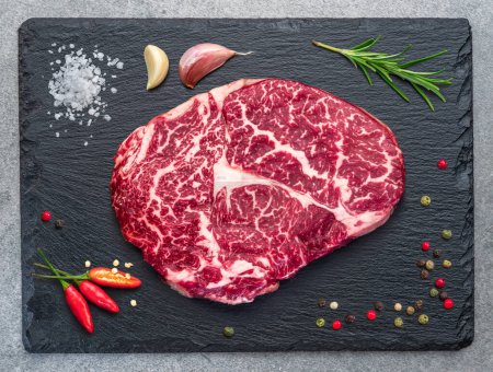 Photo for Raw ribeye steak on stone black serving plate. Flat lay. - Royalty Free Image