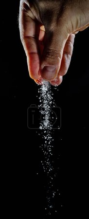 Photo for Male hand sprinkling white refined sugar crystals at black background. - Royalty Free Image