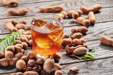Photo for Glass of cool refreshing tamarind drink and some tamarind fruit on wooden table. - Royalty Free Image