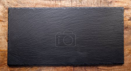 Foto de Placa de servir de pizarra negra de piedra natural sobre fondo de madera. Puesta plana. - Imagen libre de derechos