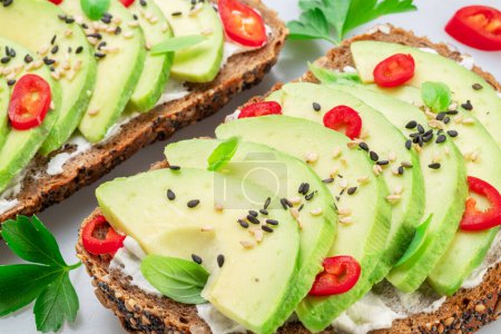 Photo for Avocado toasts - bread with avocado slices, pieces of chilli pepper and black sesame isolated on white background. - Royalty Free Image