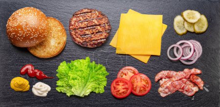 Foto de Hamburguesa con queso o ingredientes de hamburguesa en piedra natural plato de servir de pizarra negra. Puesta plana. - Imagen libre de derechos