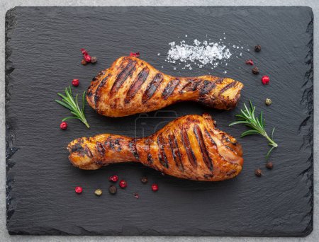 Téléchargez les photos : Grillé de délicieuses cuisses de poulet ou pilons de poulet sur une assiette de service en ardoise noire. Pose plate. - en image libre de droit