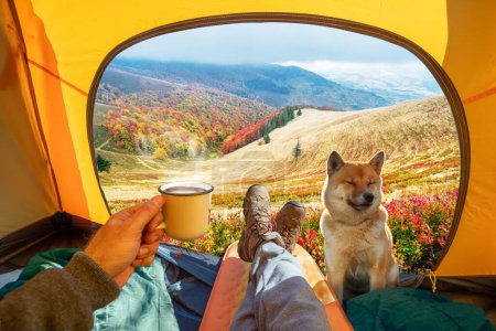 Photo for Cup of hot drink in the hand and wonderful view of autumn mountain tops through the open entrance of the tent. The beauty of a romantic hike and camping accompanied by a dog. - Royalty Free Image