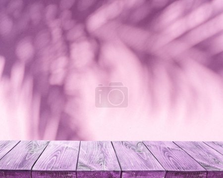 Photo for Blurred shadow of tropical palm leaves on pink wall and old planked table top in the foreground. Summer concept. - Royalty Free Image
