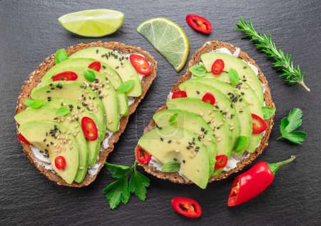 Photo for Avocado toasts - bread with avocado slices, pieces of red pepper and sesame  on black stone board. - Royalty Free Image