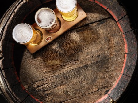 Photo for Three glasses of lager beer on old wooden barrel. Flat layer. - Royalty Free Image
