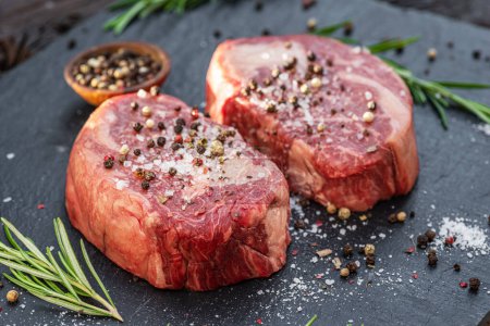 Photo for Raw Ribeye steaks with salt and herbs on grey board. Top view. - Royalty Free Image