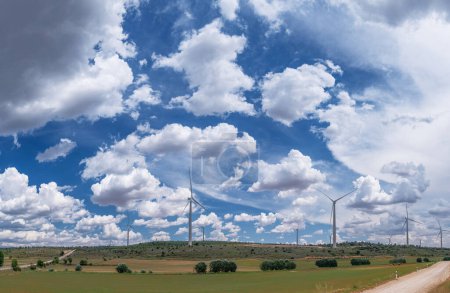 Téléchargez les photos : Des éoliennes dans un paysage rural et un ciel nuageux magnifique en arrière-plan. Production d'énergie électrique respectueuse de l'environnement. - en image libre de droit