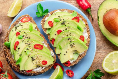 Photo for Avocado toasts - bread with avocado slices, pieces chilli pepper and black sesame on blue plate on wooden table. - Royalty Free Image