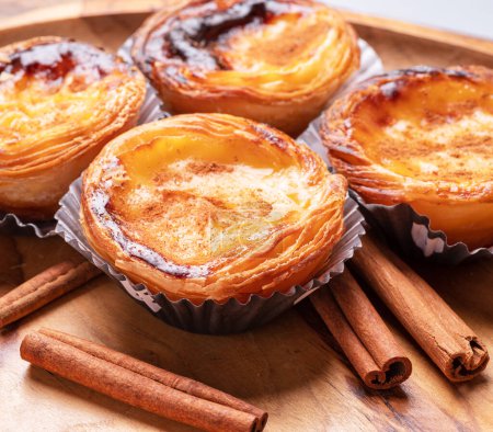 Photo for Pastel de nata tarts and cinnamon sticks on wooden tray. - Royalty Free Image