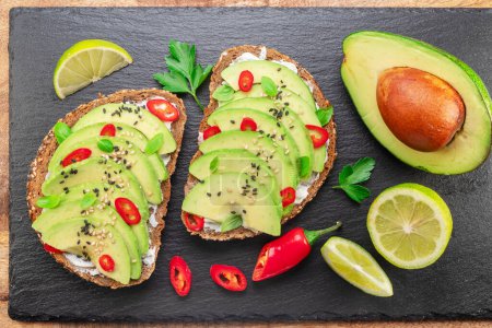 Photo for Avocado toasts - bread with avocado slices, pieces of red pepper and sesame  on black stone board. - Royalty Free Image