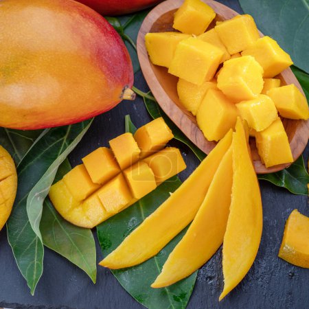 Foto de Frutas maduras de mango con rodajas y hojas de mango sobre una mesa de piedra gris. Fondo de fruta agradable para sus proyectos. - Imagen libre de derechos