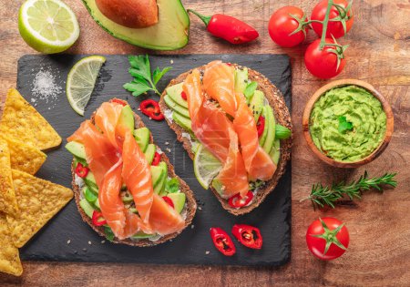 Photo for Salmon toasts - bread with salmon slices and avocado spread, guacamole and tortilla chips. Top view. - Royalty Free Image
