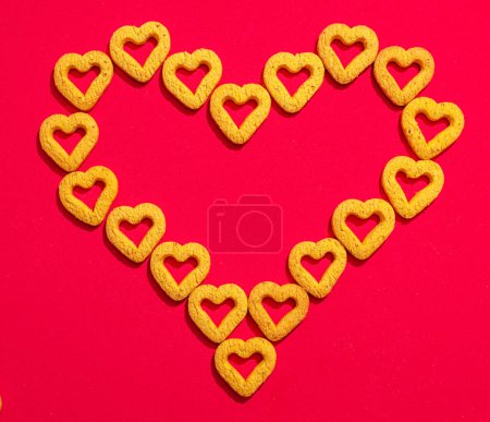 Téléchargez les photos : Les petits biscuits jaunes en forme de cœur forment un grand cœur, sur un fond rouge. Un beau fond pour la Saint-Valentin. - en image libre de droit