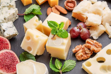 Photo for Variety of sliced cheeses with fruits, mint, nuts and cheese cutting knives. Wonderful cheese background for your projects. - Royalty Free Image
