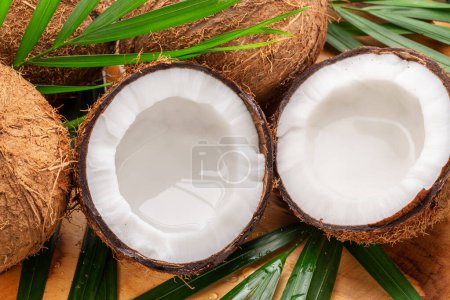 Téléchargez les photos : Des noix de coco fraîches ouvertes avec des noix de coco entières et des feuilles de noix de coco sur une table en bois. Beau fond exotique de fruits pour vos projets. - en image libre de droit