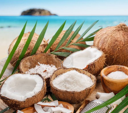 Téléchargez les photos : Des noix de coco fraîches ouvertes avec des tranches de noix de coco, des flocons et des feuilles de noix de coco sur fond d'océan exotique. Beau fond de fruits pour vos projets. - en image libre de droit