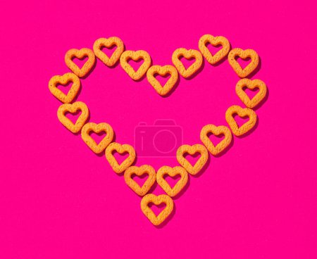 Téléchargez les photos : Les petits biscuits jaunes en forme de cœur forment un grand cœur, sur fond rose. Un beau fond pour la Saint-Valentin. - en image libre de droit