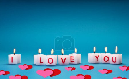 Téléchargez les photos : "Je t'aime "imprimé sur des bougies brûlantes sur un fond bleu. Ci-dessous se trouvent de nombreux cœurs roses et rouges. Beau fond pour la Saint-Valentin. - en image libre de droit