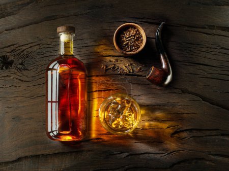 Foto de Un vaso de whisky, una botella de whisky y una pipa de tabaco en una vieja mesa de madera. Vista superior. - Imagen libre de derechos