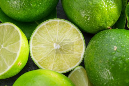 Téléchargez les photos : Fruits de lime mûrs avec des tranches et des feuilles de lime sur une table en pierre grise. Beau fond d'agrumes de fruits pour vos projets. - en image libre de droit