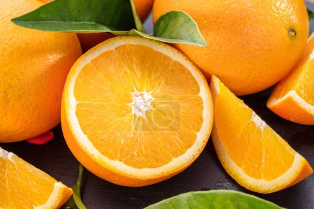 Foto de Frutos anaranjados maduros con rodajas y hojas de naranjo sobre una mesa de piedra gris. Fondo de fruta agradable para sus proyectos. - Imagen libre de derechos