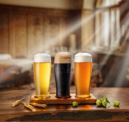 Foto de Set de diferentes vasos de cerveza refrigerada sobre mesa de madera. Borroso interior de pud anticuado en el fondo. - Imagen libre de derechos