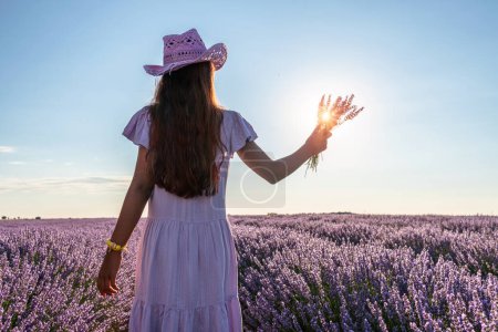 Photo for Girl walking in the lavender field and holding lavender bouquet in her hand. Brihuega, Spain. - Royalty Free Image