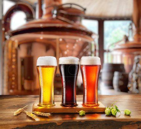 Téléchargez les photos : Ensemble de verres de bière différente sur table en bois et système de brassage en cuivre flou à l'arrière-plan. - en image libre de droit