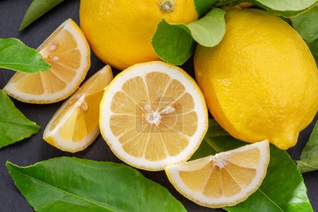 Photo for Ripe lemon fruits with slices and lemon leaves on a gray stone table. Nice fruit citrus background for your projects. - Royalty Free Image