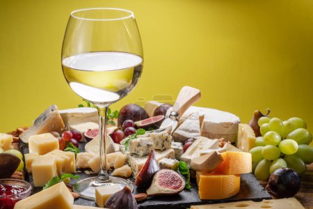 Foto de Copa de vino blanco con variedad de quesos en rodajas con frutas, menta, nueces y cuchillos de corte de queso. Maravilloso fondo de vino y queso para sus proyectos. - Imagen libre de derechos