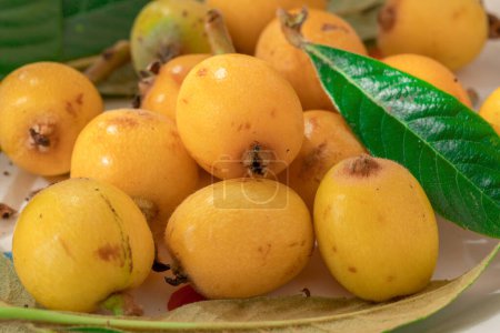 Loquats fruits with green leaves on plate close up.