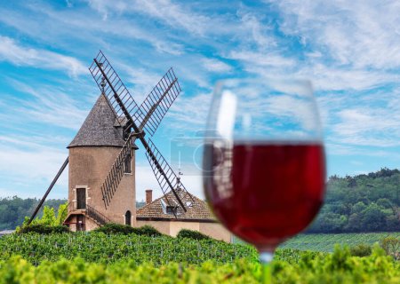 Verre flou de vin rouge au premier plan et moulin éponyme de vin rouge français célèbre en arrière-plan. Romanche-Thorines. 