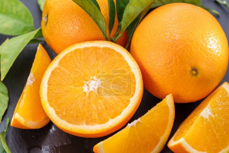Foto de Frutos anaranjados maduros con rodajas y hojas de naranjo sobre una mesa de piedra gris. Fondo de fruta agradable para sus proyectos. - Imagen libre de derechos