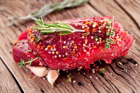 Téléchargez les photos : Steaks de boeuf cru avec des herbes et des épices prêtes à cuire sont sur une planche de bois. - en image libre de droit