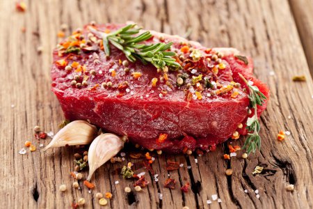 Photo for Raw beef steaks with herbs and spices ready for cooking are on wooden board. - Royalty Free Image
