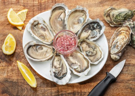 Photo for Opened raw oysters with sauce and lemon slices on plate on wooden table. Top view. - Royalty Free Image