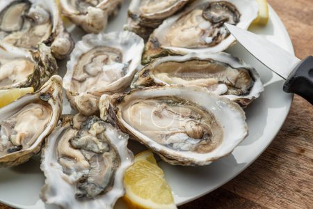 Photo for Opened raw oysters with sauce and lemon slices on plate on wooden table. Top view. - Royalty Free Image