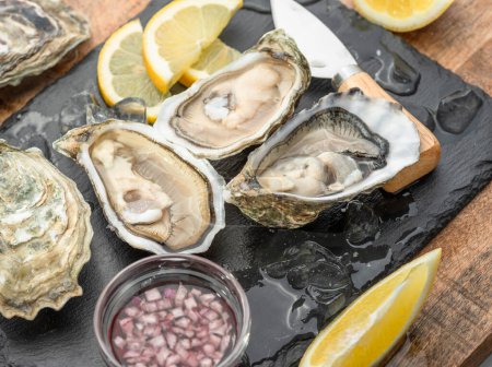 Photo for Opened raw oysters with sauce and lemon slices on gray stone serving board. Delicacy food. - Royalty Free Image