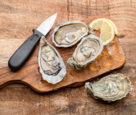 Photo for Three opened raw oysters and oyster knife on wooden table. Top view. - Royalty Free Image