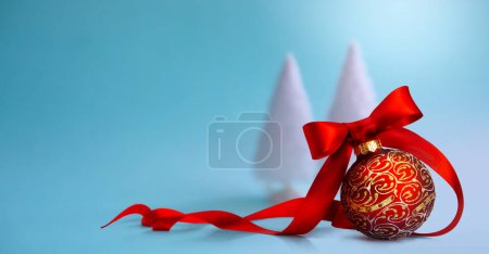 Foto de Primer plano de una bola roja de Navidad atada con cinta y árbol de Navidad en una mesa. Diseño de banner o tarjeta de felicitación con spac de copia - Imagen libre de derechos