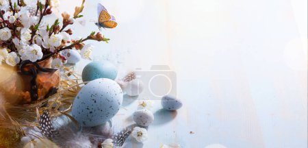 Foto de Feliz Pascua; Huevos de Pascua y flores de ramita sobre fondo de mesa azul - Imagen libre de derechos