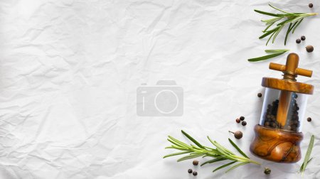 Foto de Coctelera de pimienta italiana tradicional y hojas de romero orgánico verde sobre fondo de papel culinario blanco. Ingrediente, especia para cocinar. colección de banner culinario desig - Imagen libre de derechos