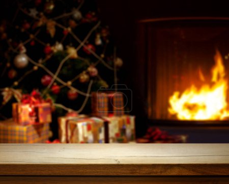 Foto de Mesa de madera vacía sobre fondo de Navidad desenfocado con árbol de Navidad, regalos y chimenea; espacio libre para su decoración. - Imagen libre de derechos
