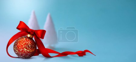 Foto de Primer plano de una bola roja de Navidad atada con cinta y árbol de Navidad en una mesa. Diseño de banner o tarjeta de felicitación con spac de copia - Imagen libre de derechos