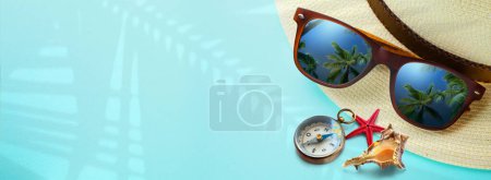 Foto de Concept vacation and summer travel banner. Happy holidays on tropical sea beach. Panama hat, compass, sunglasses with a reflection of the sandy trovic beach and palm tree - Imagen libre de derechos